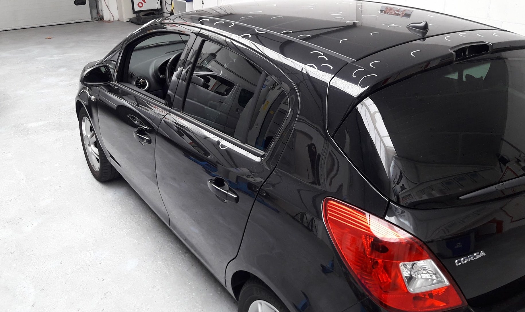 Zwarte Opel Corsa in de witte werkplaats, met markeringen op het dak